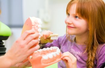 Dentist explaining girl how to brush her teeth Johns Creek, GA