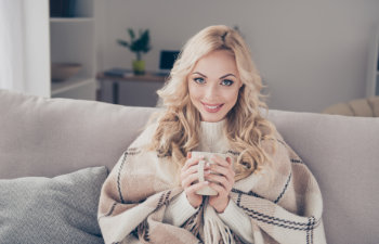 woman sitting on divan wrapped in warm cover light white interior room, 