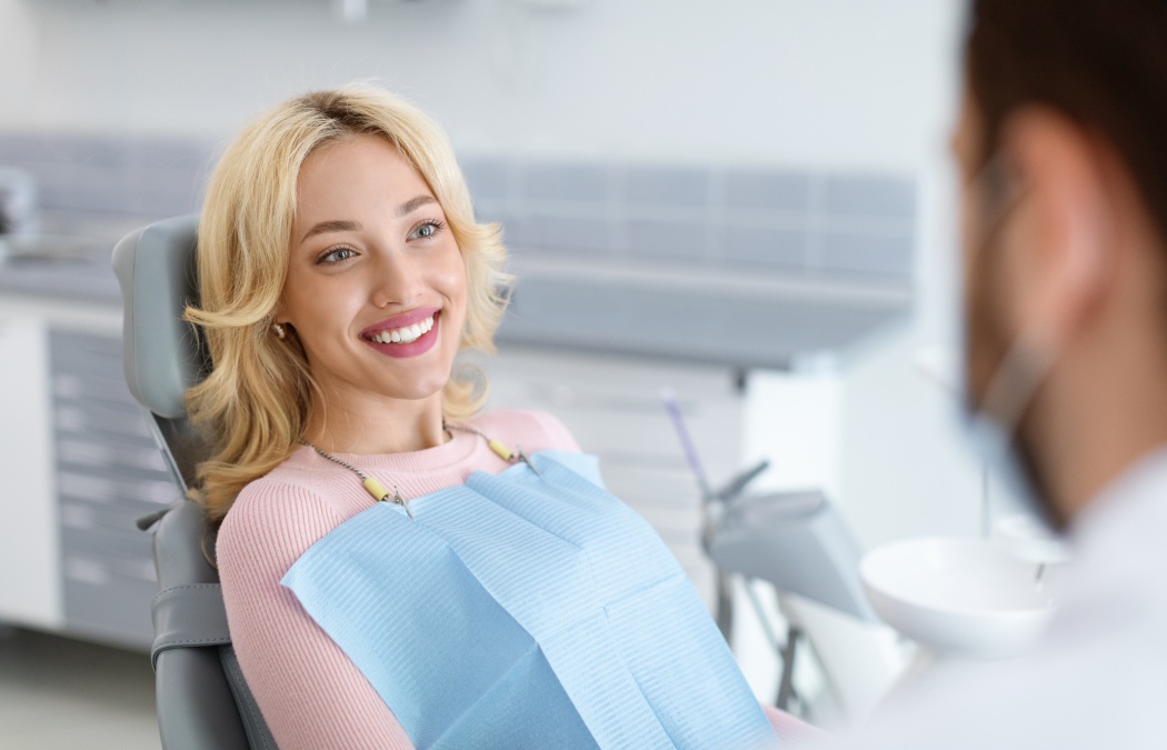 Relaxed blonde woman smiling to her dentist, side view, copy space. Peaceful pretty young lady having conversation with her doctor stomatologist, enjoying modern treatment at new dental clinic, 