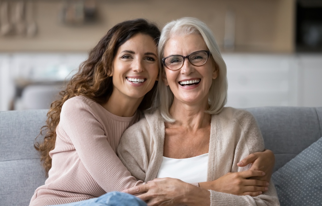 Portrait of two beautiful young and mature females, different generations women hugging sit on sofa, sharing warmth, joyful moments together. Family ties, intergenerational connection, love, support, 